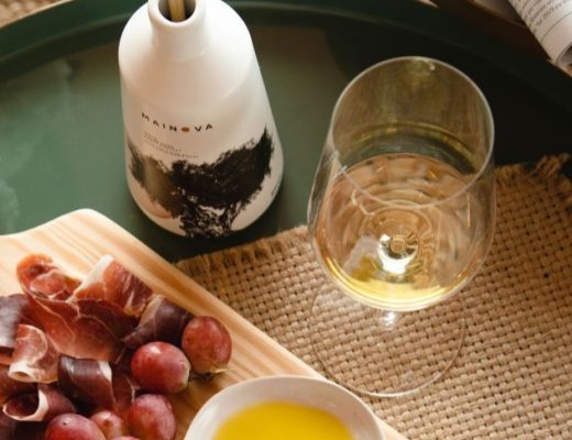 Azeite da marca Mainova sobre mesa com vinho e tábua de entradas