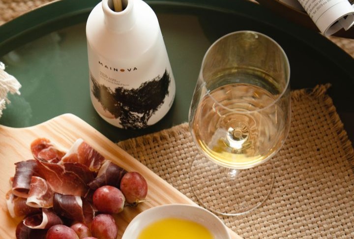 Azeite da marca Mainova sobre mesa com vinho e tábua de entradas